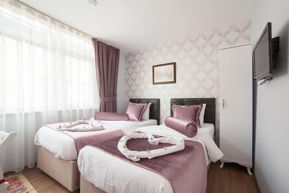 A hotel room with two beds, a TV, and a window with curtains.
