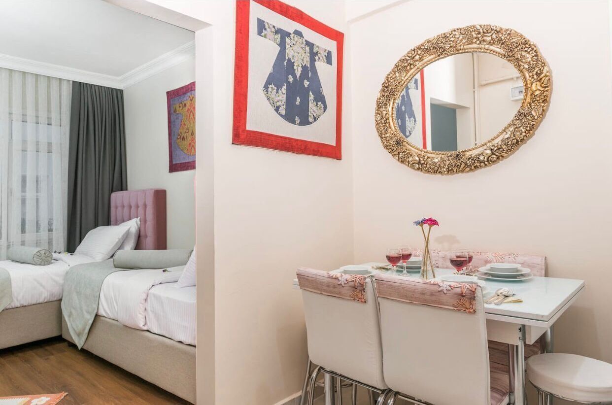 A hotel room with a bed, a dining table with chairs, a mirror, and artwork on the walls.