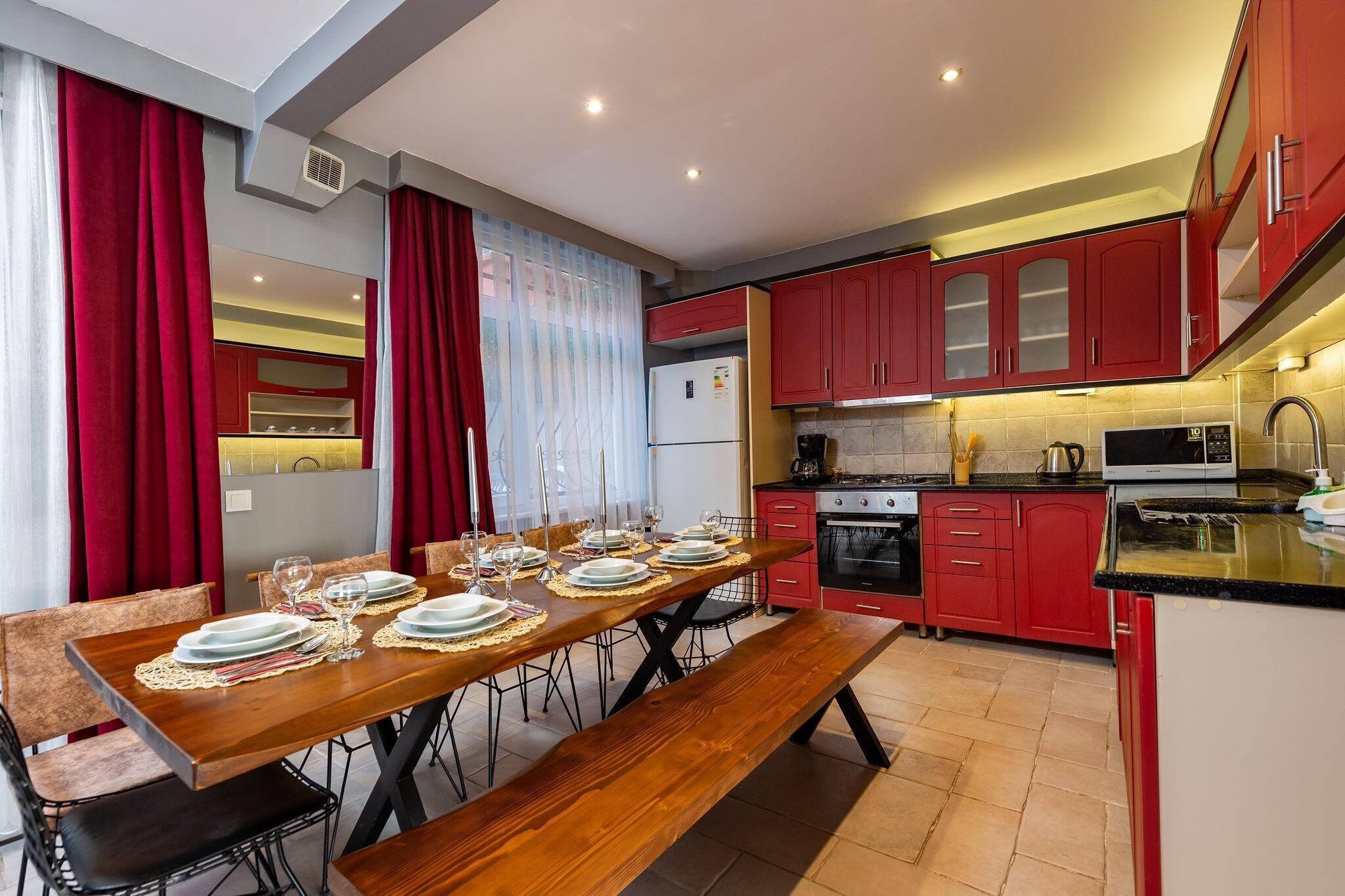 Una cocina moderna con armarios rojos, una mesa de comedor preparada para seis comensales y un horno empotrado.