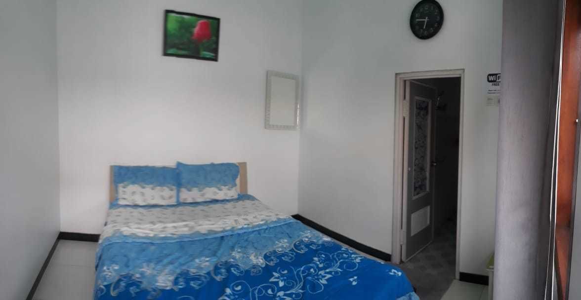 A bedroom with a bed, a wall clock, a framed picture, and a door.