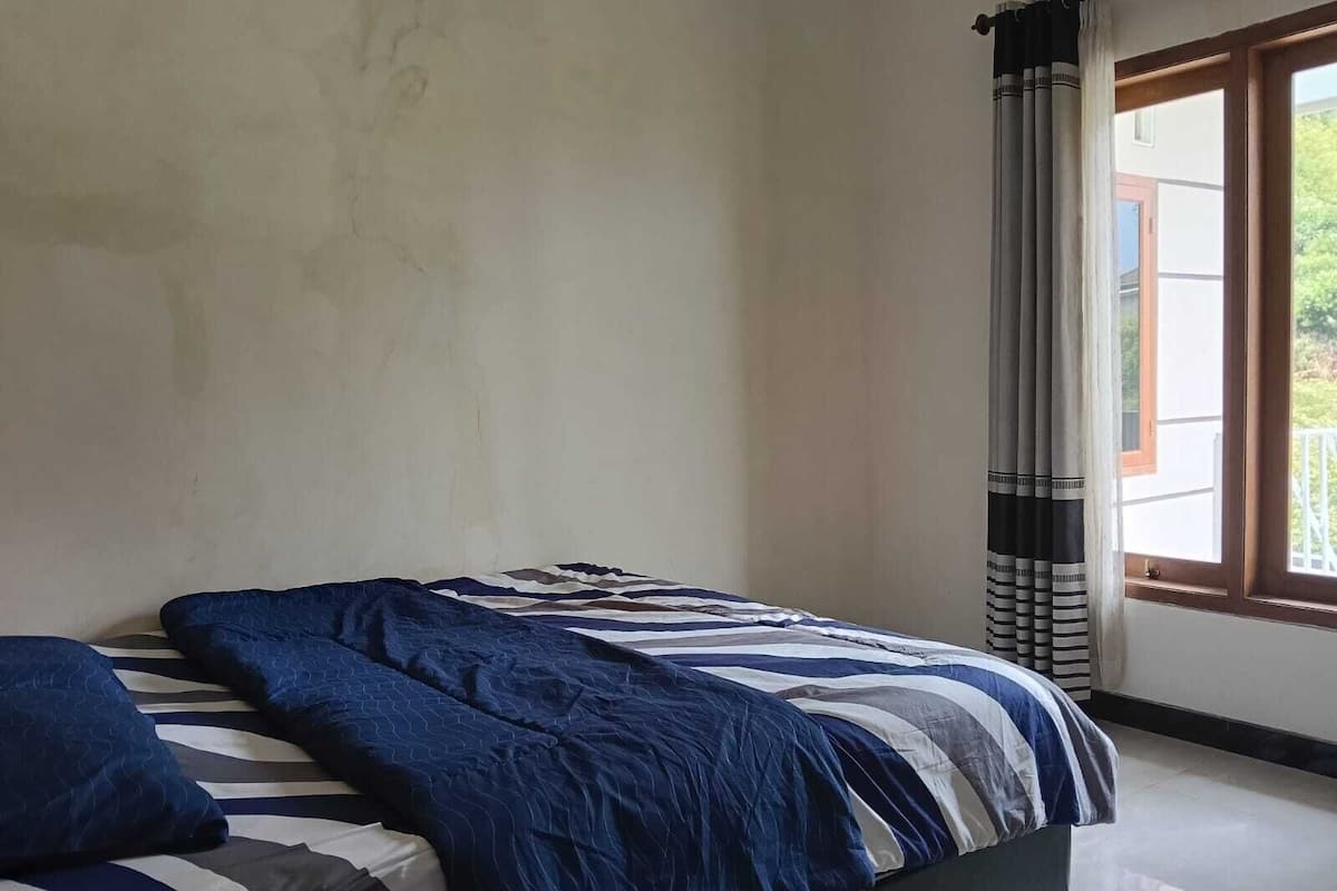 A bedroom with a bed, a window with curtains, and a view of the outside.