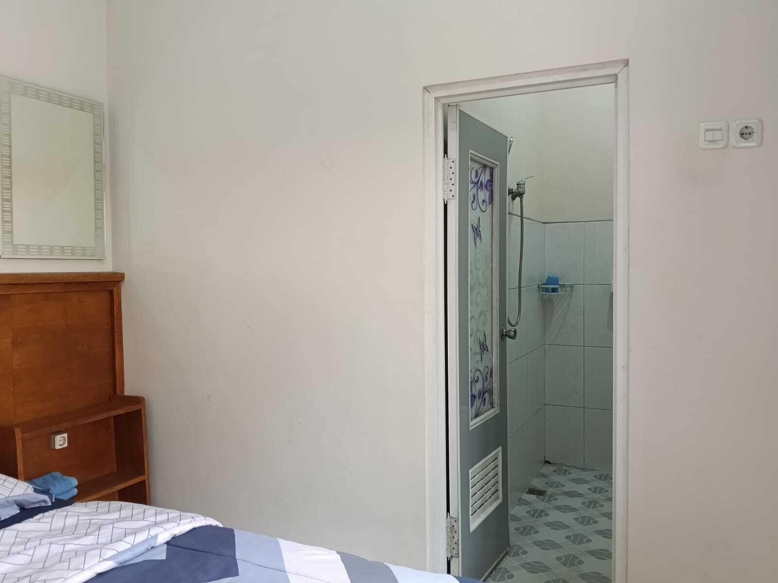Une chambre à coucher avec une tête de lit en bois, un lit recouvert d’une couvre-lit à motifs et une porte donnant sur une salle de bain équipée d’une douche et dont les murs sont recouverts de carreaux.