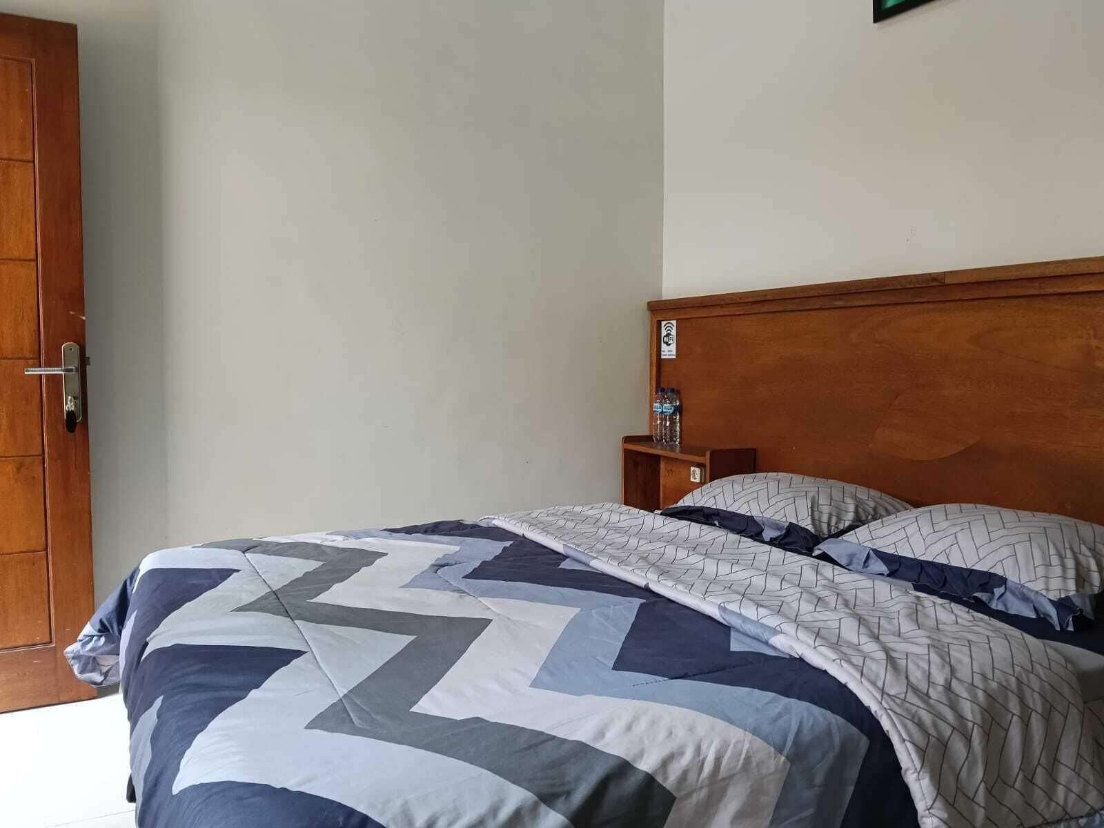 A bedroom with a wooden headboard, a bed with a patterned quilt, and a small shelf with water bottles.