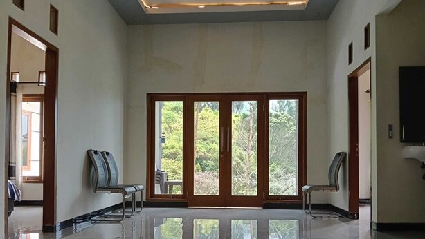Una habitación amplia con piso de baldosas brillantes, puertas correderas de vidrio que dan a vistas de vegetación, y dos sillas.