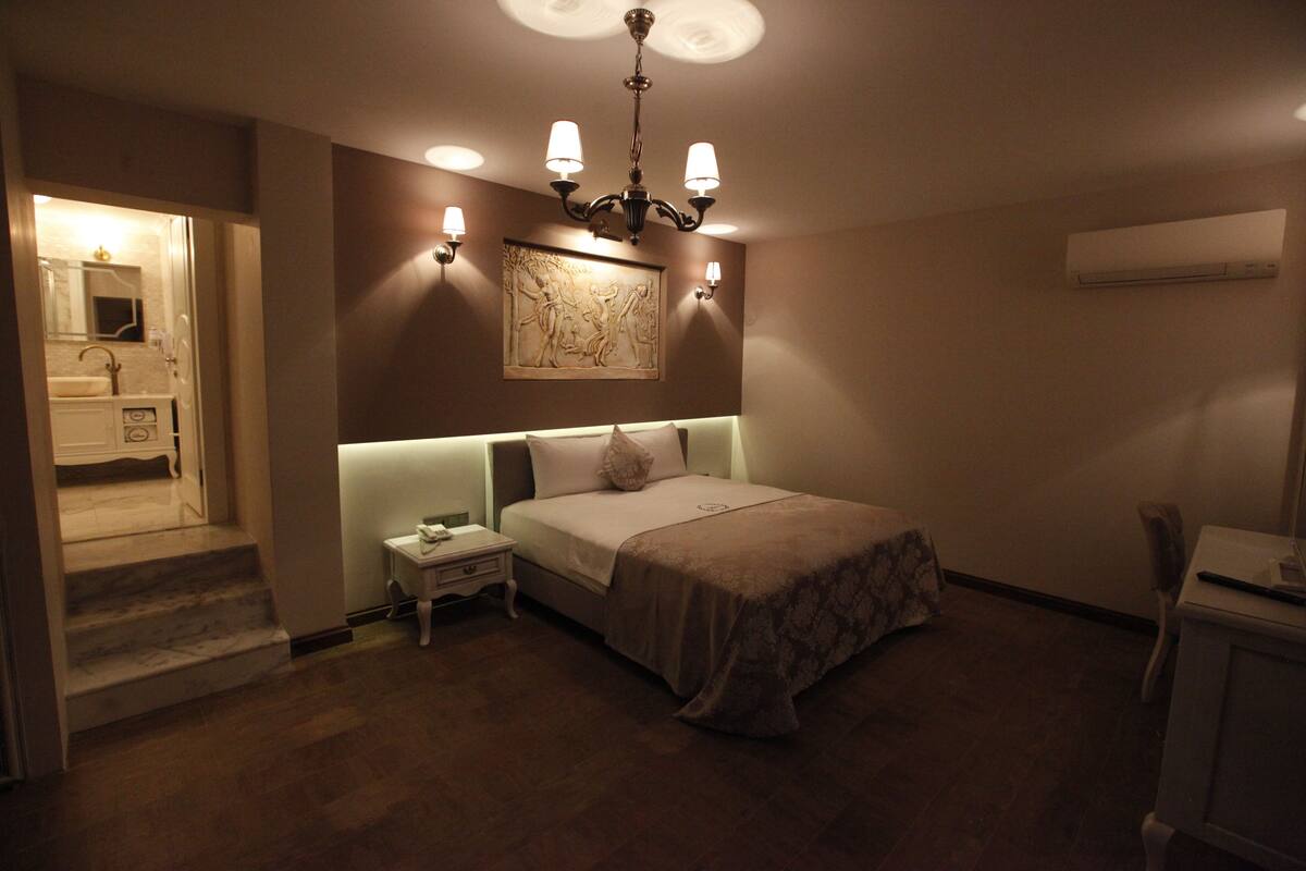 A bedroom with a bed, bedside table, nightstand, and a chandelier.