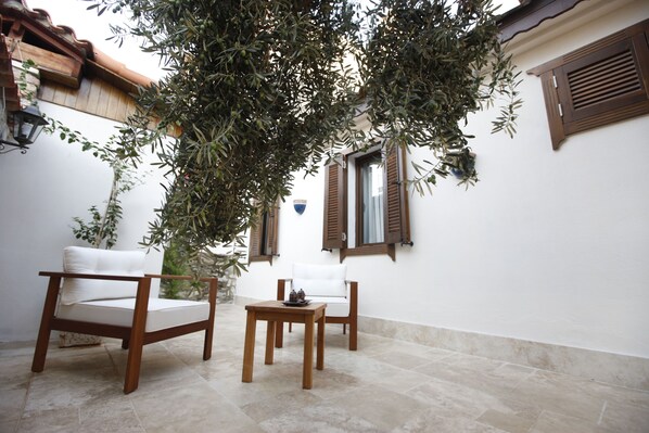 A patio with two wooden chairs and a small table, surrounded by white walls and wooden shutters.