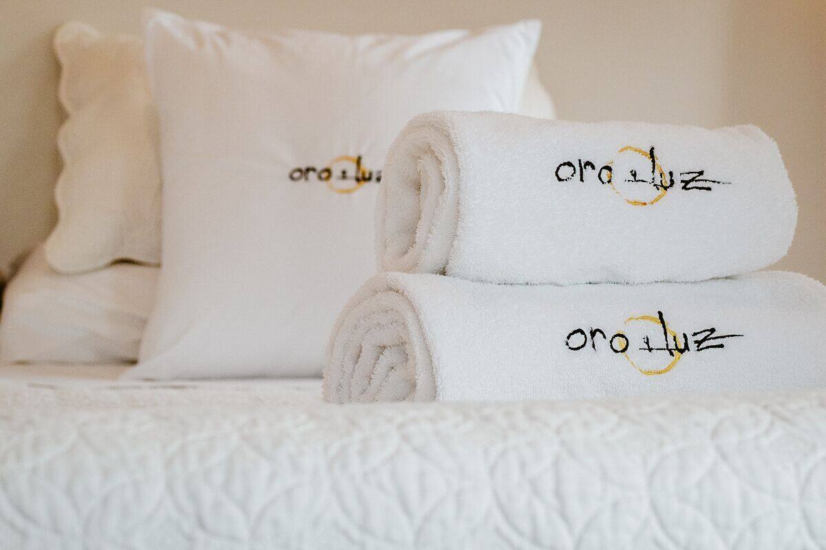 A neatly made bed with rolled white towels and pillows, each with embroidered text.