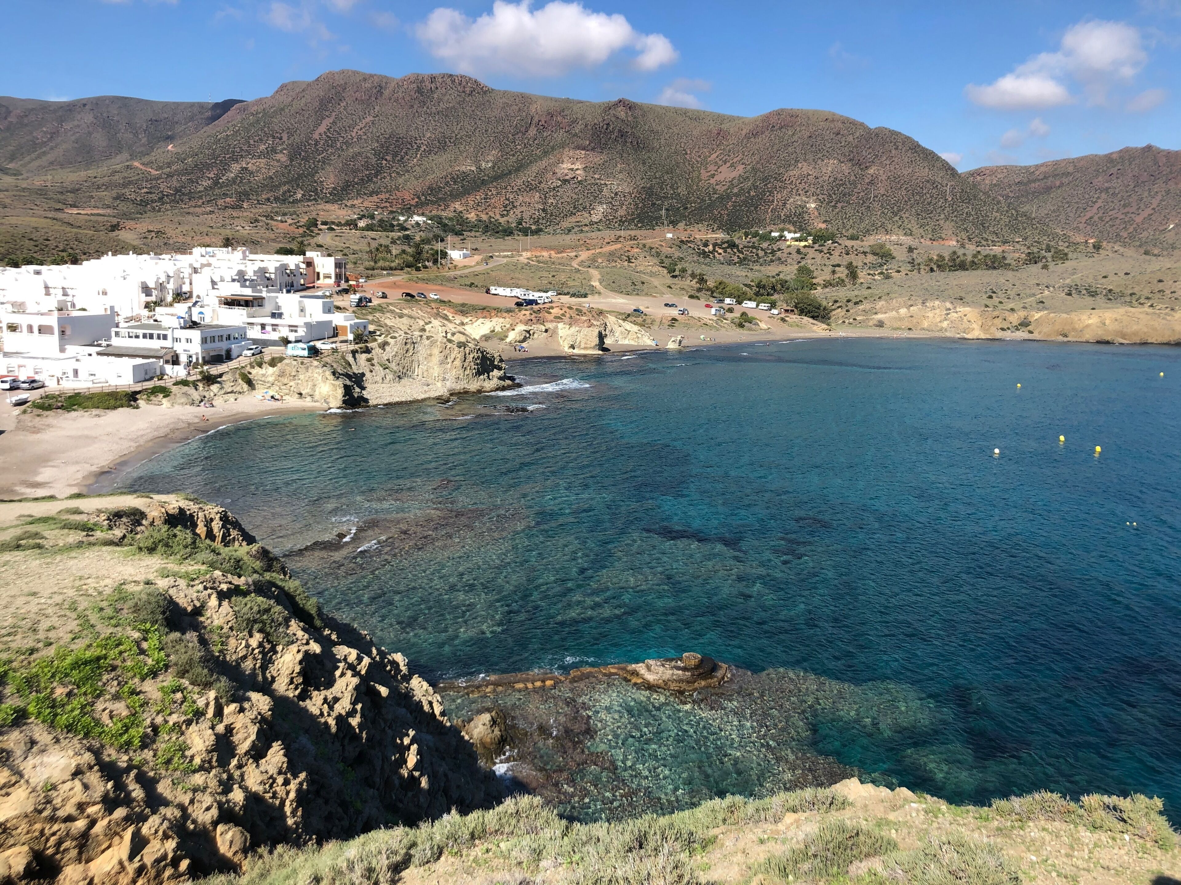 Un pueblo costero con edificios blancos, una playa y montañas al fondo.