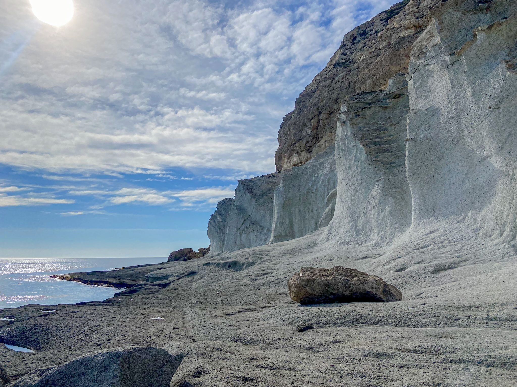 A coastal landscape with a rocky beach, a large boulder, and a cliff.