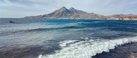 A coastal scene with clear skies, a mountain in the background, and calm sea waves.