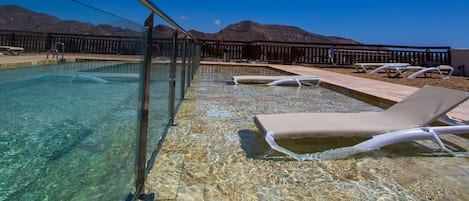 Une piscine aux eaux cristallines, bordée de chaises longues et d’une terrasse en bois, le tout entouré de montagnes.