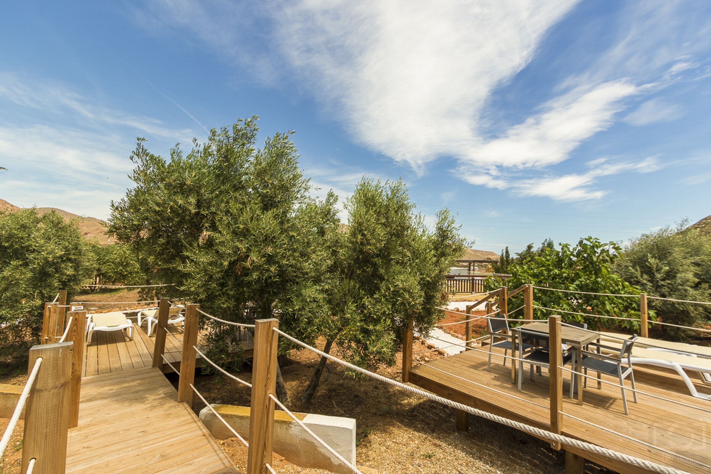 Eine Holzterrasse mit Sitzgelegenheiten und einem Seilgeländer.