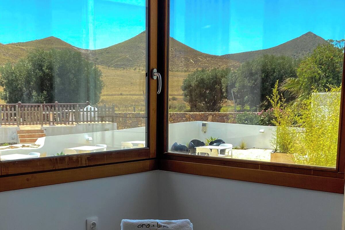 A hotel room with a large window offering a view of a mountainous landscape. There are two neatly folded towels on the bed.