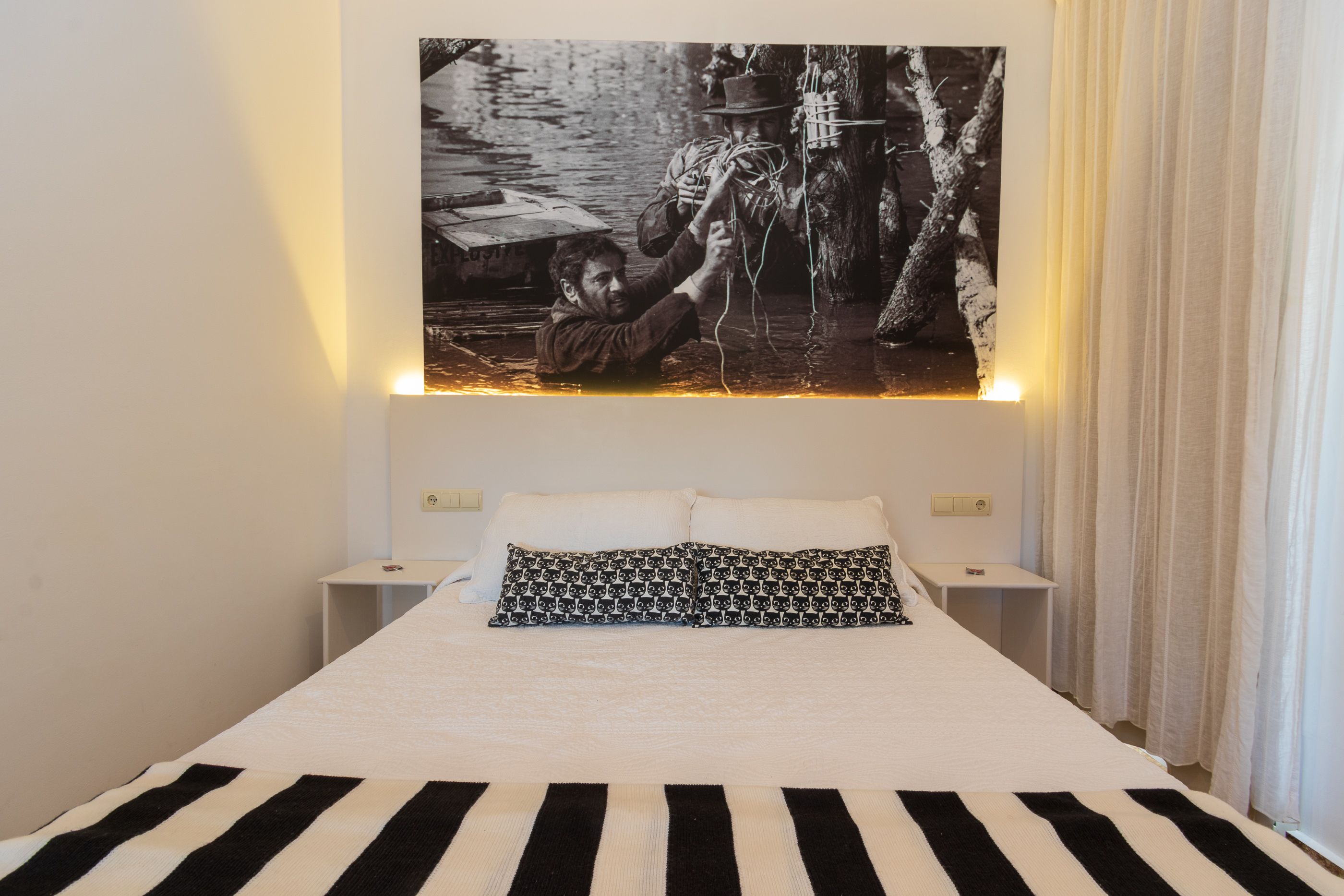 Una cama con una colcha a rayas negras y blancas, dos almohadas blancas y una almohada con estampado negro y blanco.