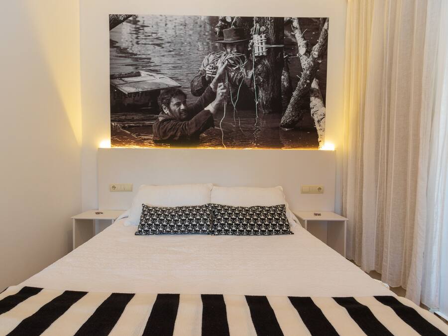Una cama con una colcha a rayas negras y blancas, dos almohadas blancas y una almohada con estampado negro y blanco.