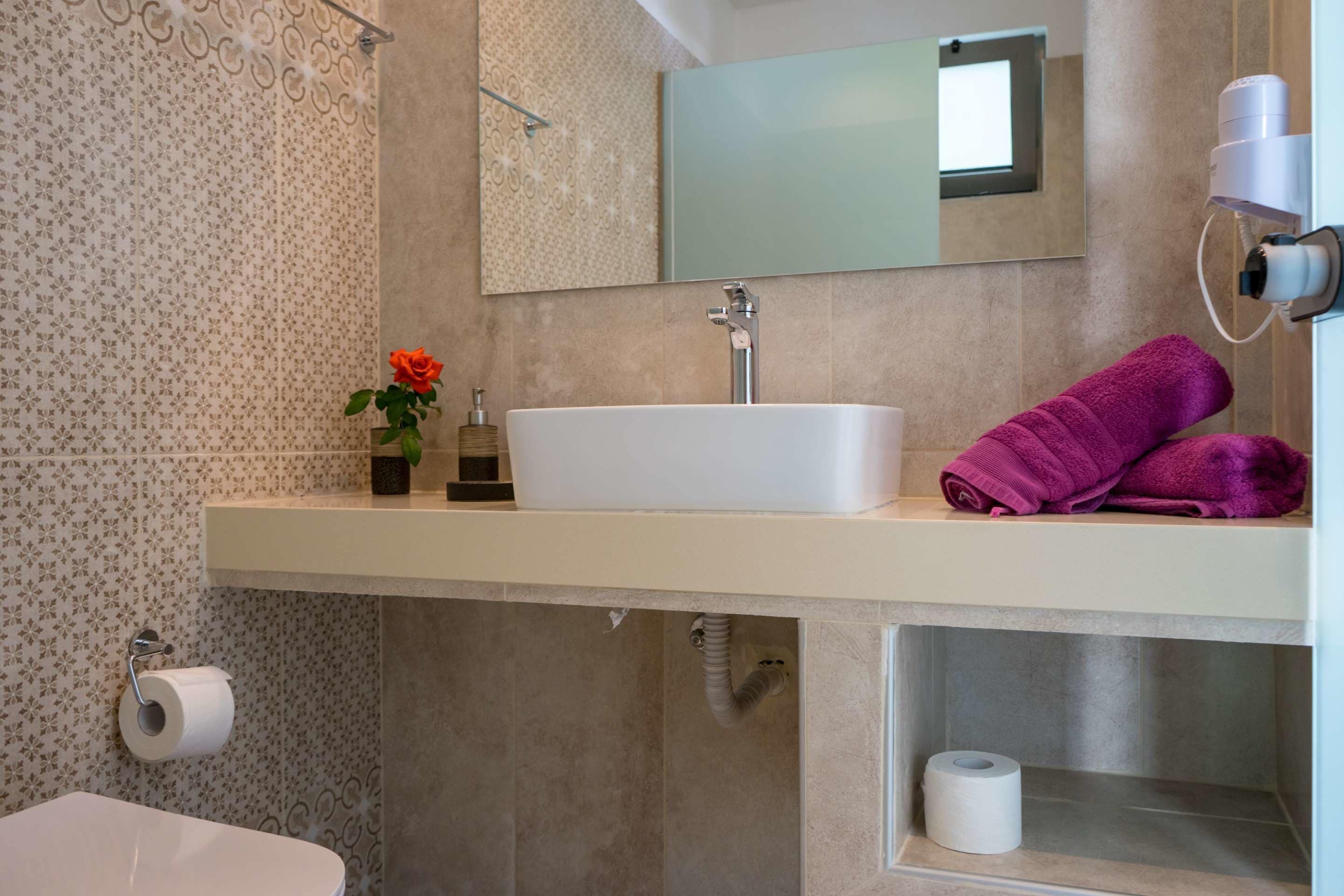 Ein Badezimmer mit Waschbecken, Spiegel, Handtuchhalter und Toilette.