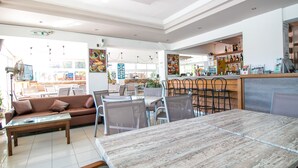 A modern cafe with a wooden table and chairs, a sofa, and a counter with various items. - Stamos Hotel (Rhodes)