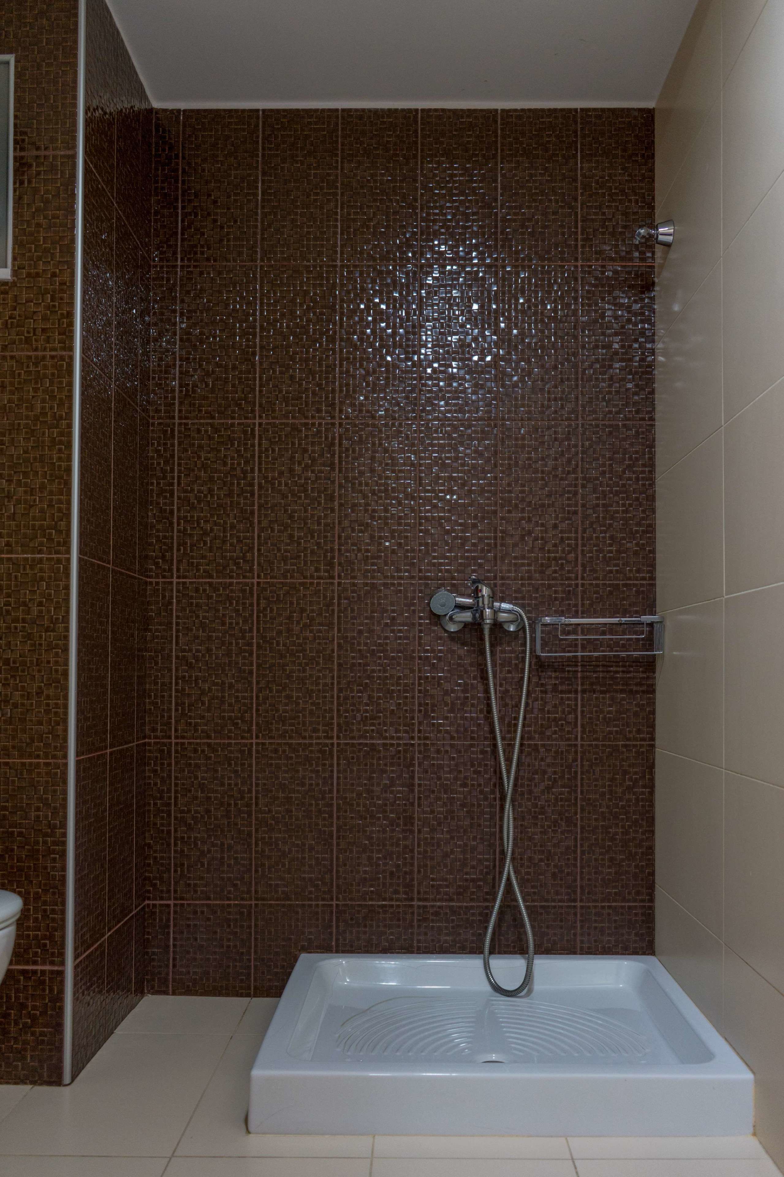 A shower with a rectangular tub, brown tiled walls, and a chrome showerhead.