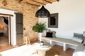 A cozy room with a stone wall, a wooden bench, a hanging black lamp, and a round table with a candle. - Can Sastre Boutique Hotel (Sant Antoni de Portmany)