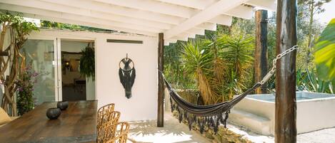 A wooden dining table with chairs, a hammock, and a stone wall.