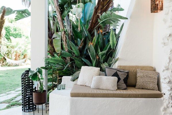 Uma área de estar aconchegante com um banco estofado, cercada por plantas tropicais exuberantes e um lustre.