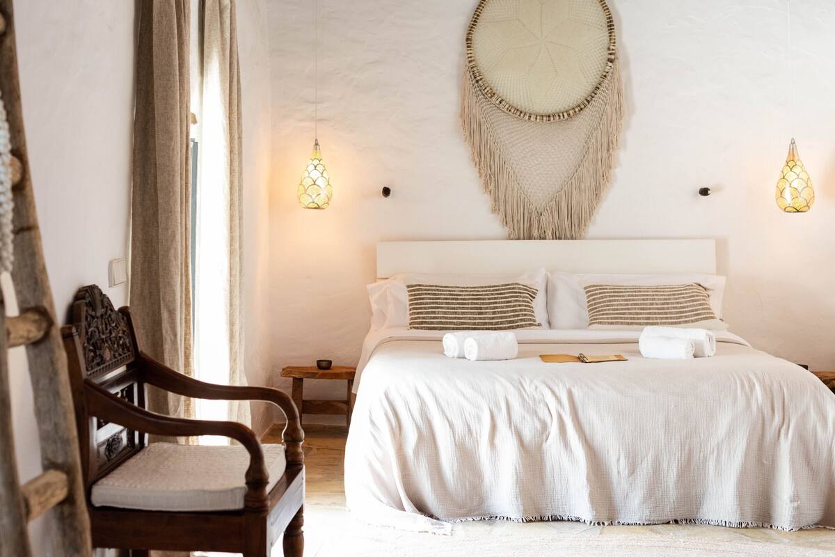 A neatly arranged bedroom with a large bed, a wooden chair, and a wall hanging.