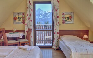 Una habitación con dos camas, una mesa de madera con un florero, y vistas a las montañas a través de una ventana.