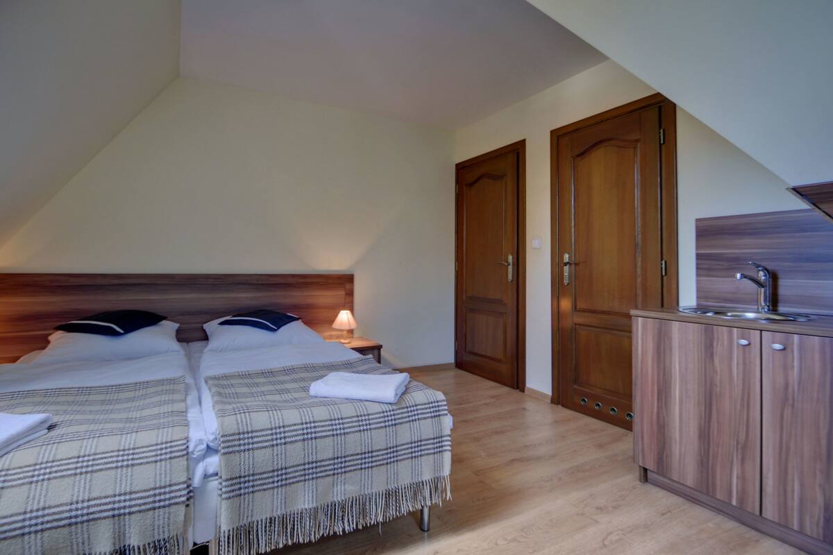Un dormitorio con dos camas, un armario de madera y una pequeña kitchenette.