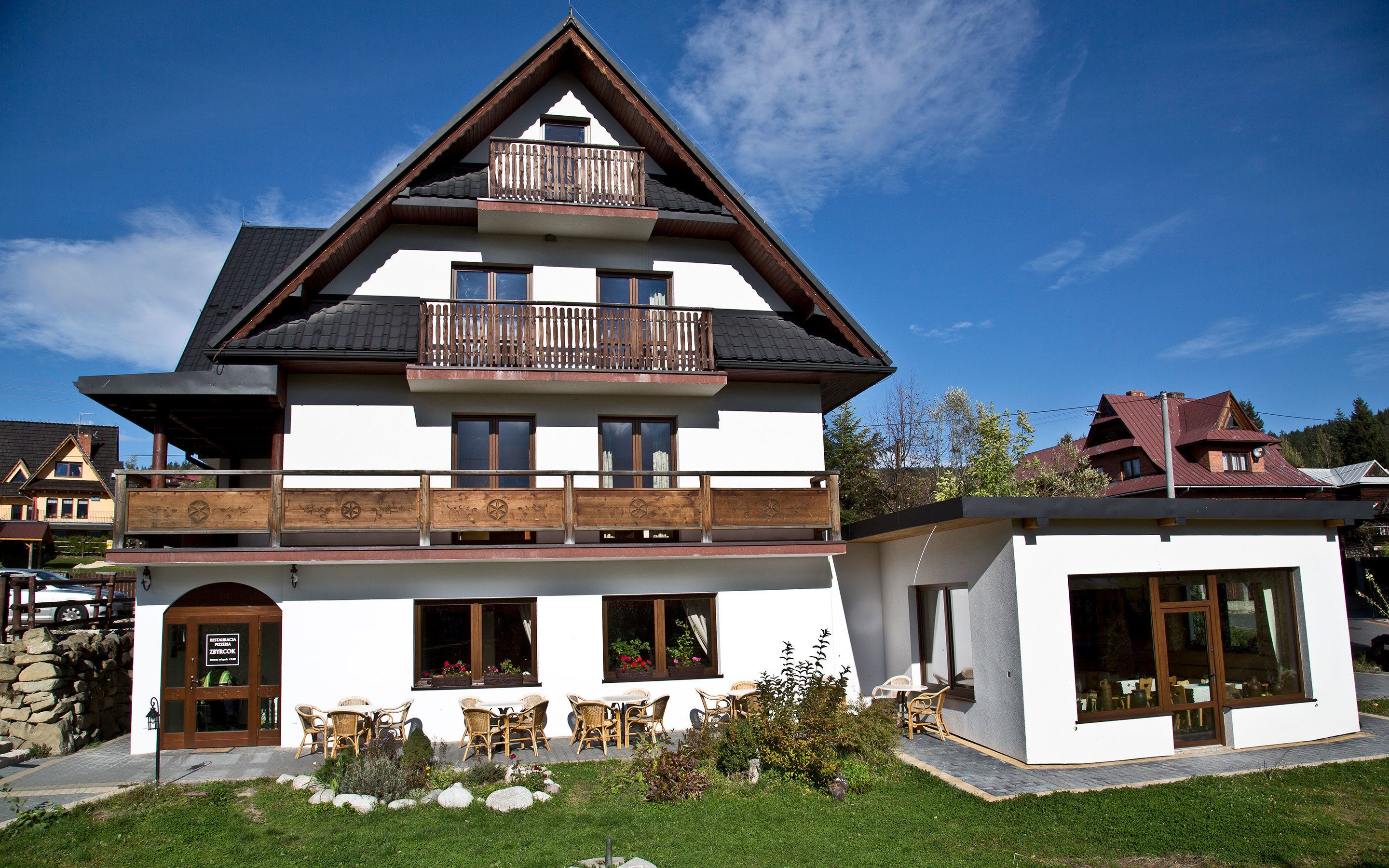 A two-story building with a balcony, large windows, and outdoor seating.