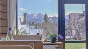 Una habitación con un banco de madera, una planta en maceta y vistas de montañas nevadas a través de un ventanal grande.