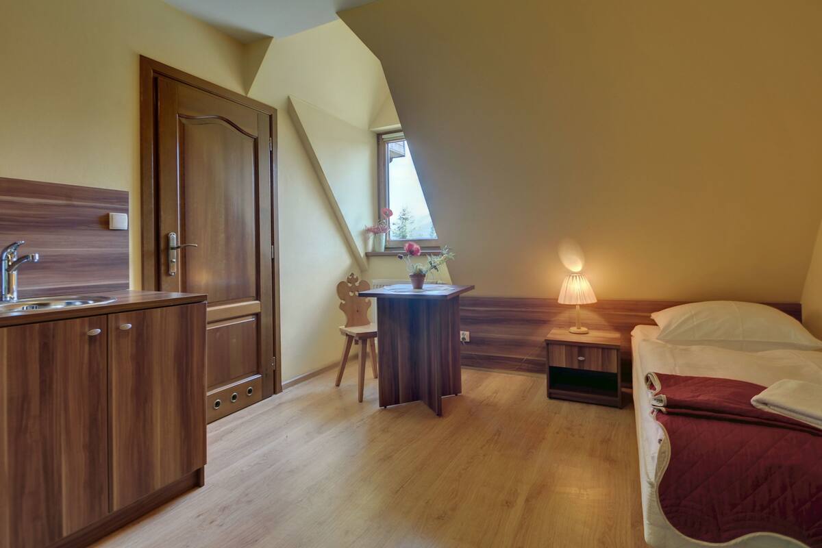 Un dormitorio con cama, mesita de noche, lámpara y un pequeño escritorio con silla.
