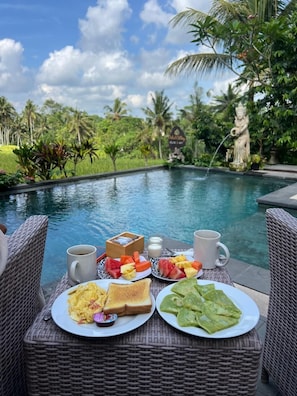 Un buffet de petit-déjeuner installé au bord d’une piscine, dans un cadre tropical.