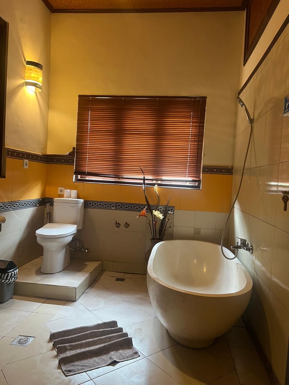 A bathroom with a toilet, bidet, bathtub, and a window with blinds.