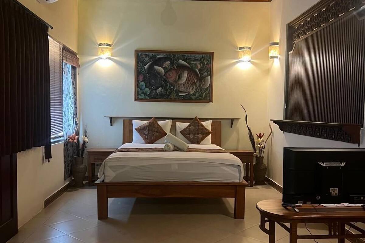 Een slaapkamer met een bed, een televisie en een schilderij aan de muur.