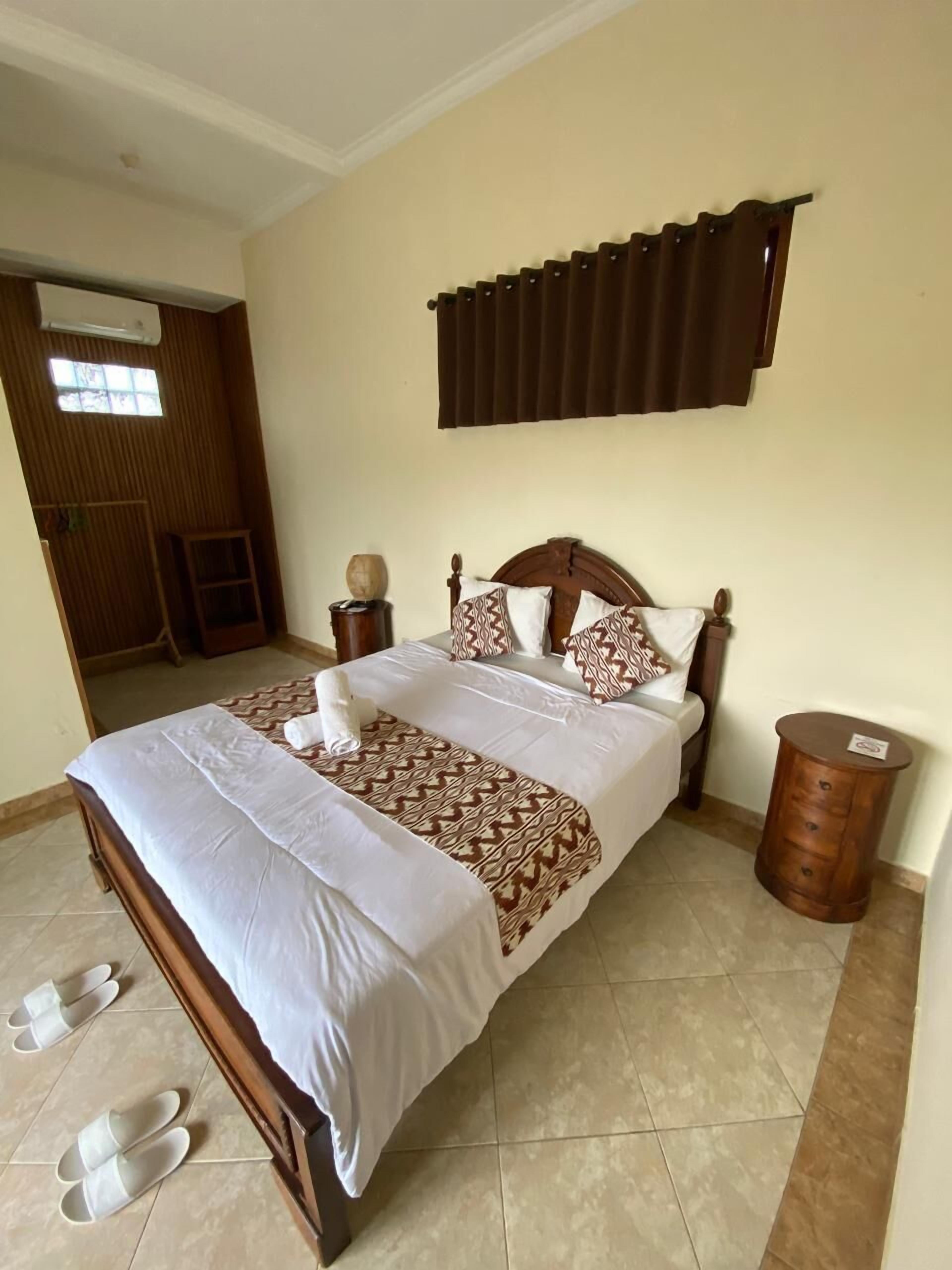 Un lit bien fait, avec une couvre-lit à motifs, une tête de lit en bois et deux tables de chevet ornées d’objets décoratifs.