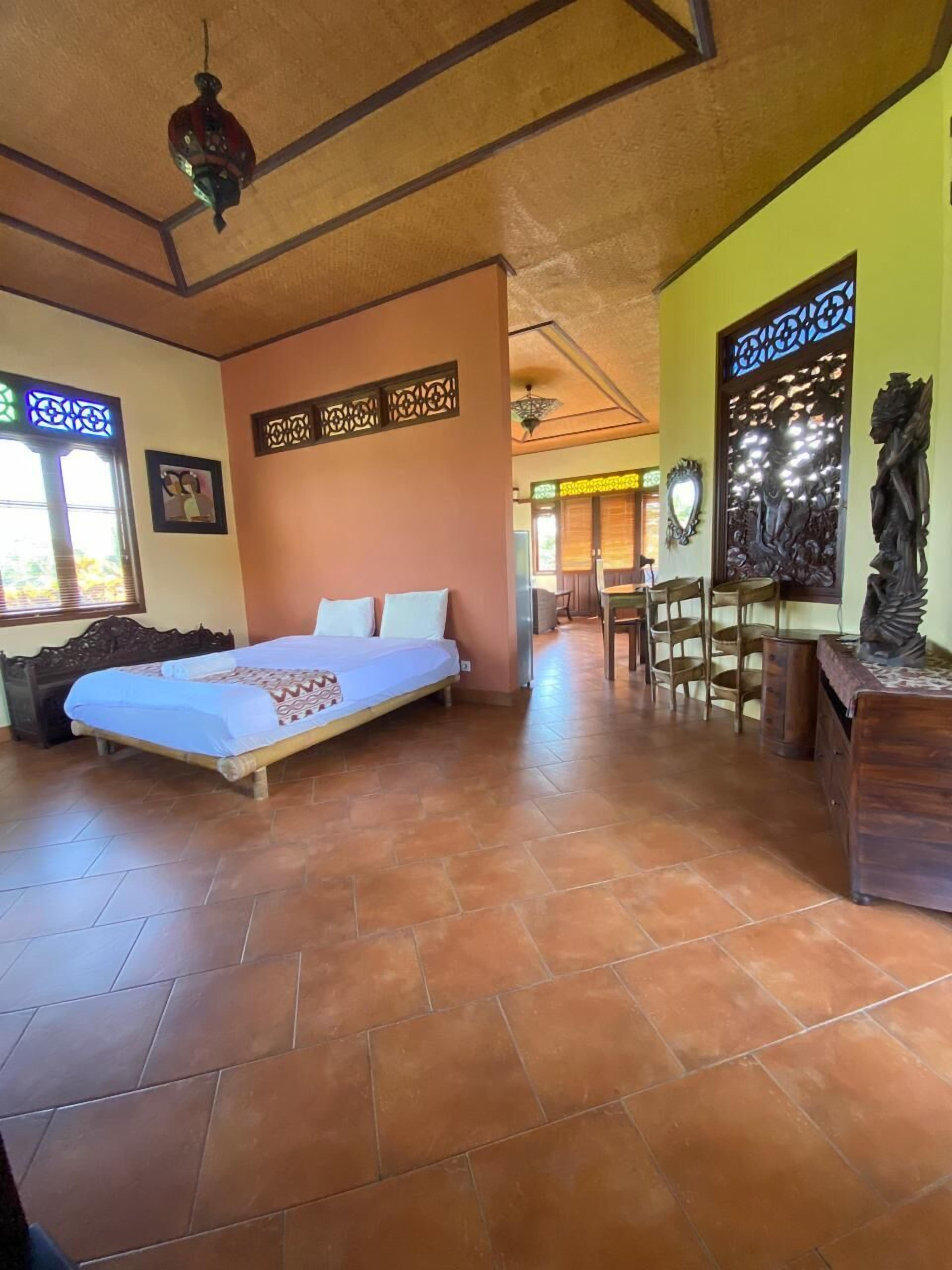 A bedroom with a bed, a desk, and a chair. There is a window with a decorative screen and a wall with a carved wooden panel.