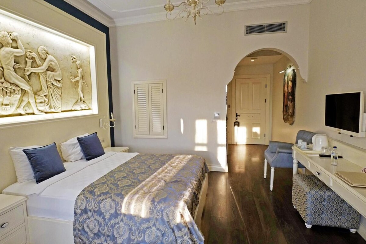 A hotel room with a large bed, a desk with a chair, a television, and a decorative wall piece.