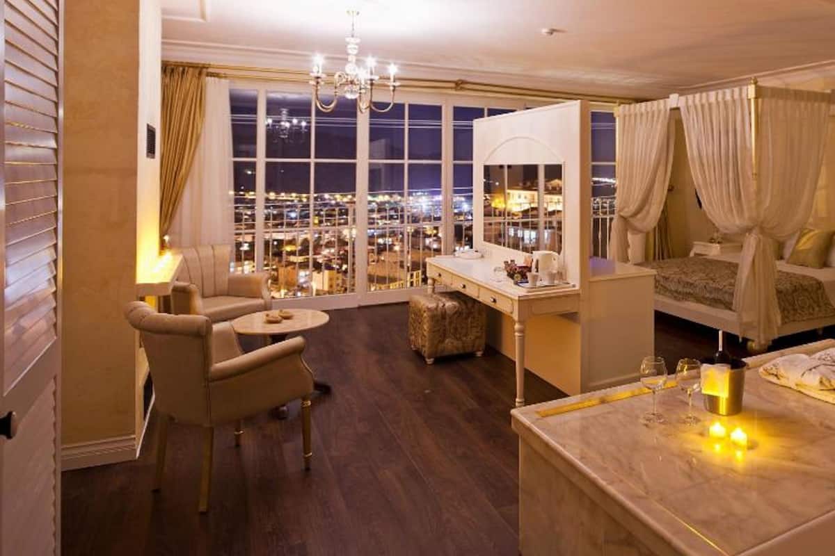 Habitación de hotel con un ventanal grande, un escritorio, una silla, una cama con cortinas y una araña.