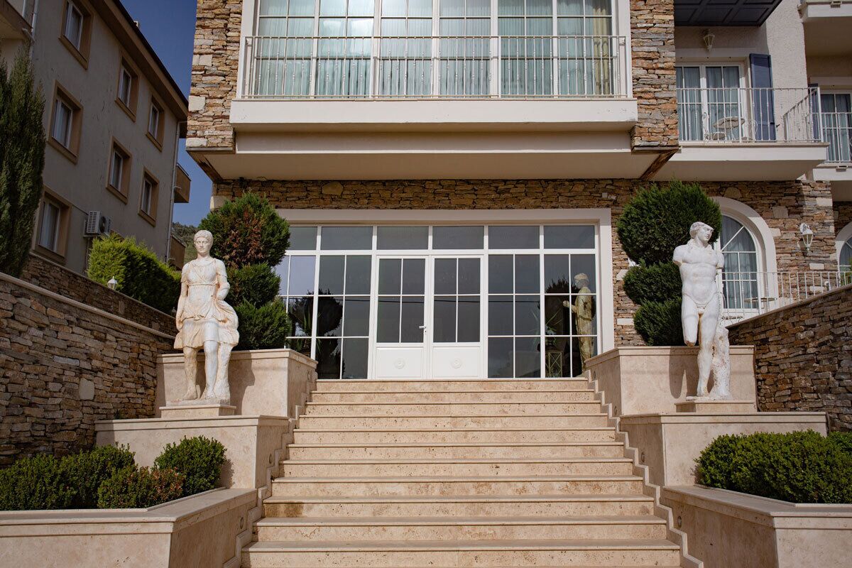A building with a stone facade, a large entrance with double doors, and two statues on the steps.