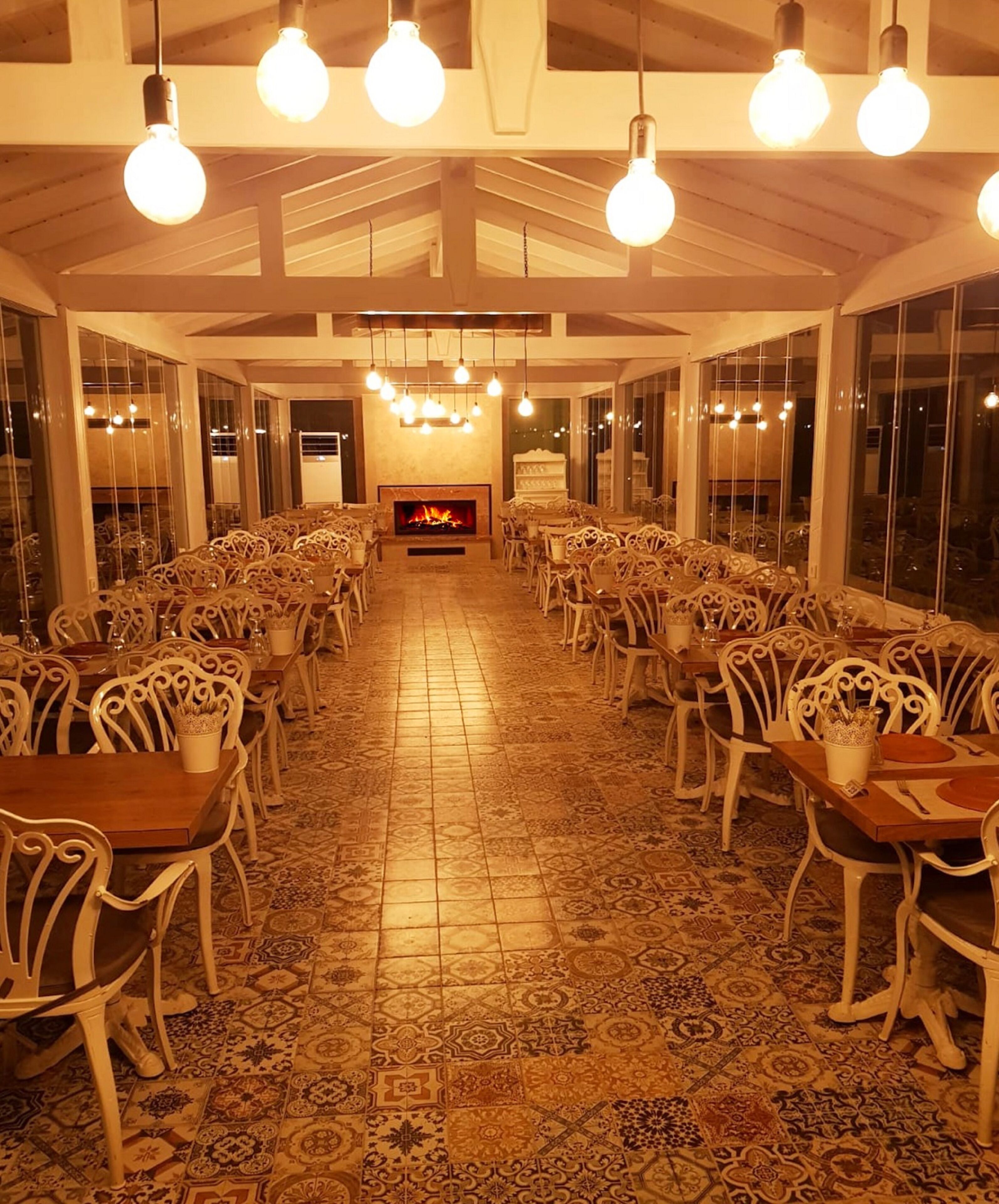 Un comedor amplio con sillas y mesas blancas de detalles ornamentales, suelo estampado y chimenea en el centro.