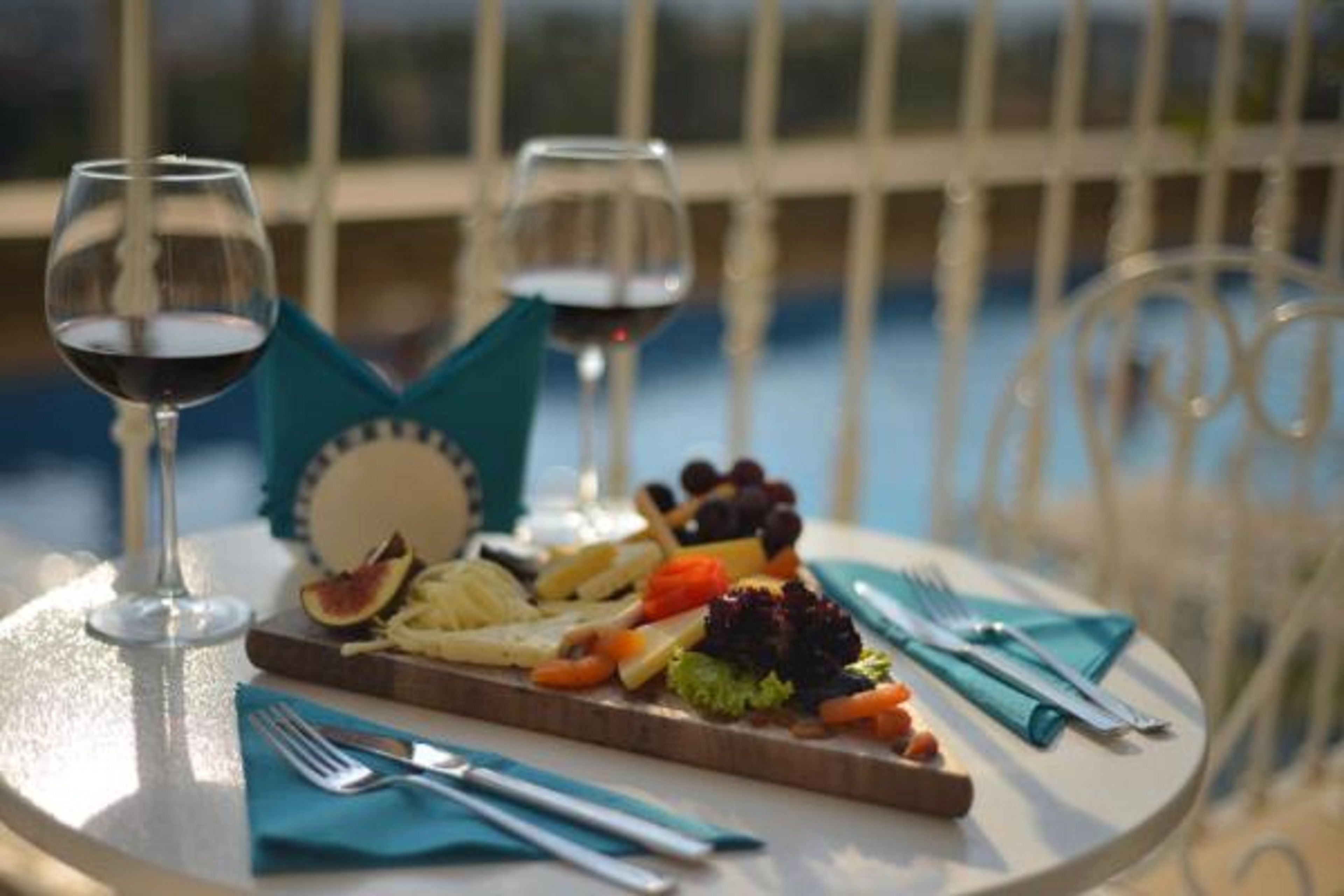 Una mesa con una tabla de quesos, dos copas de vino y vista a una piscina.