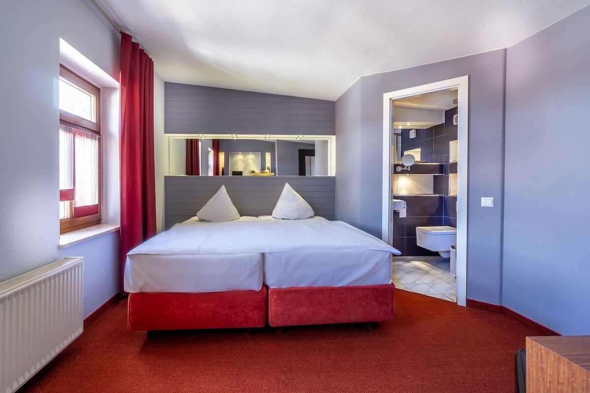 Hotelkamer met een tweepersoonsbed, een ingebouwde kaptafel met spiegel, een raam met rode gordijnen en een rode vloerbedekking.