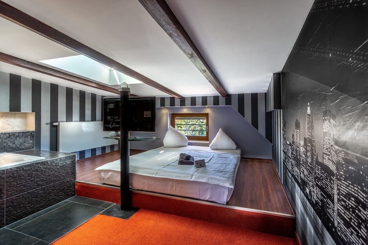 Een moderne hotelkamer met dakraam, een bed met witte lakens, een stadsgezichtsmural en een klein bureau.