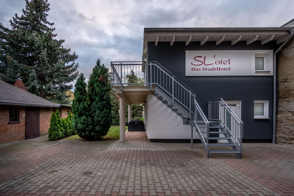 Een modern hotel met een trap die leidt naar een overdekt gebied, omringd door groen en een metselpad.