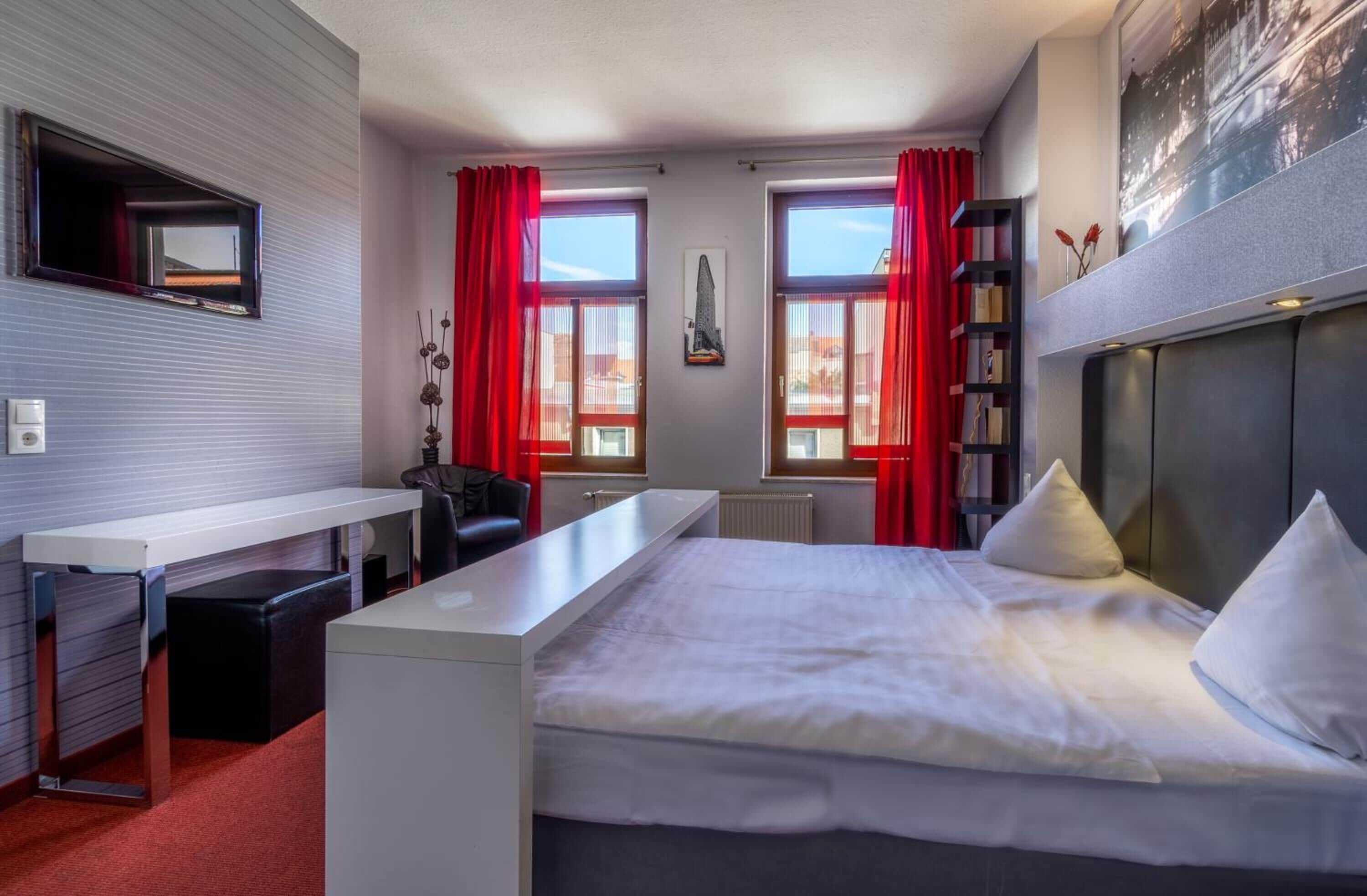Una habitación de hotel moderna con una cama grande, un escritorio, una silla y un televisor montado en la pared.