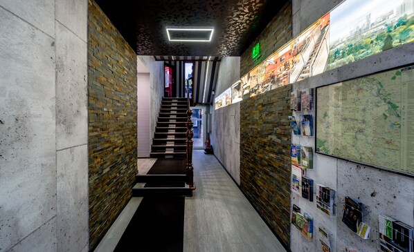 Un pasillo estrecho con una pared de ladrillo a un lado y otra pared con un mapa y folletos. Una escalera conduce a una puerta al final.