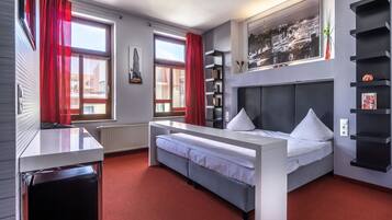 A modern hotel room with a bed, a desk, and a bookshelf.
