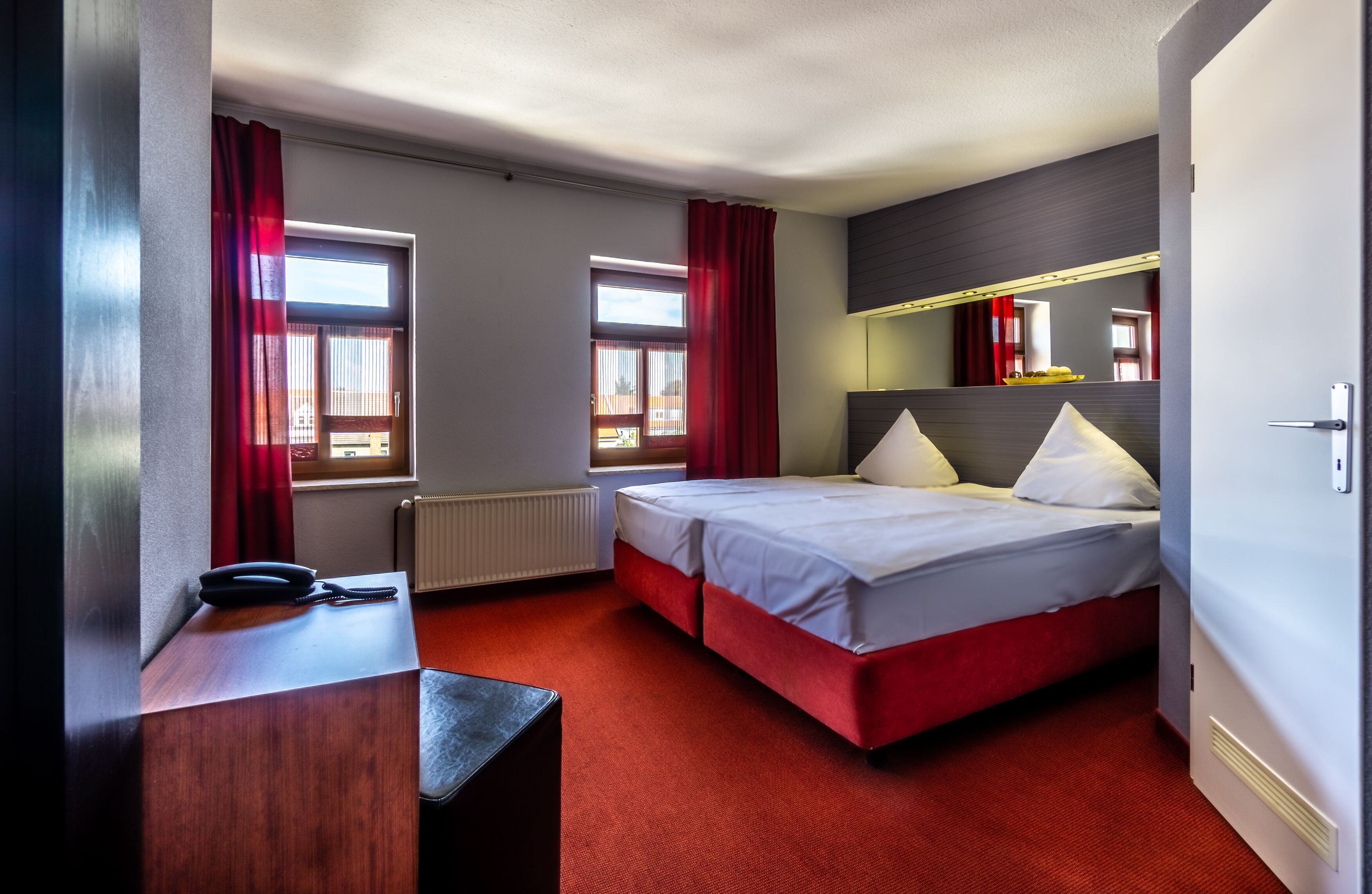 A hotel room with a bed, a desk, a telephone, and a mirror.