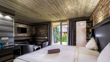 Habitación de hotel moderna con techo de madera, pared de piedra, televisor de pantalla plana, cama con ropa blanca y vistas al exterior.