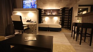 A modern hotel room with a cityscape view, a desk with a chair, a sofa, and a TV on the wall. - SL'otel - Budget (Bernburg)